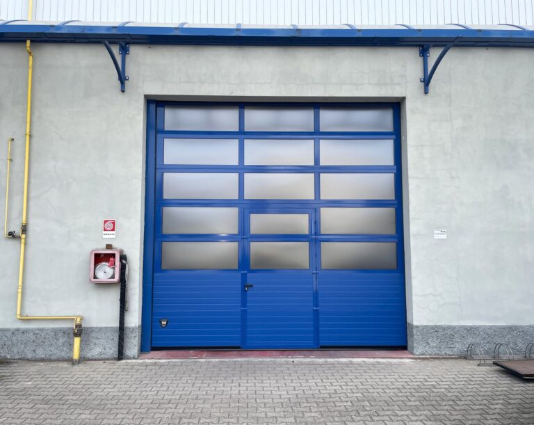 Porta sezionale industriale, con sezioni finestrate e porta pedonale.