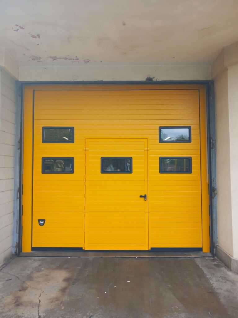 Porta sezionale industriale, con oblò e porta pedonale inserita
