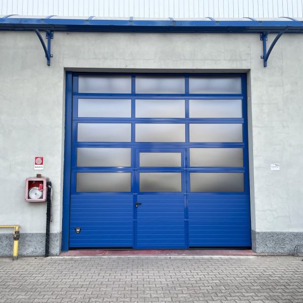 Porta sezionale industriale, con sezioni finestrate e porta pedonale.