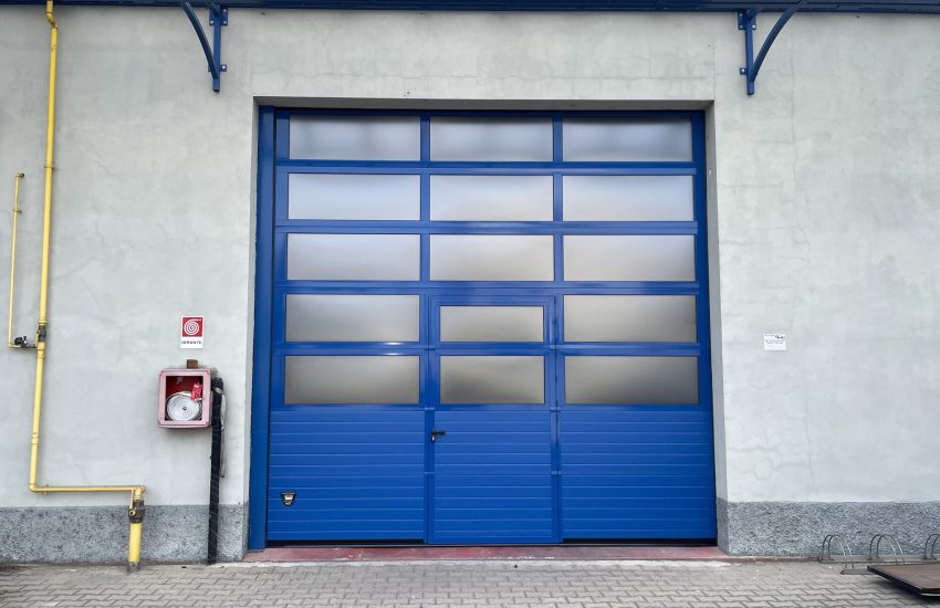 Porta sezionale industriale, con sezioni finestrate e porta pedonale.