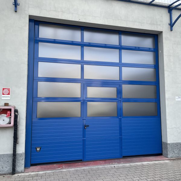 Porta sezionale industriale, con sezioni finestrate e porta pedonale.